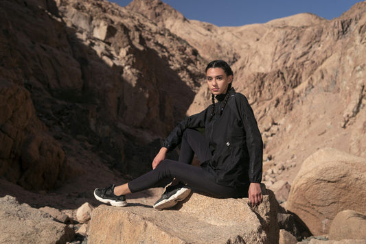 A woman sitting on a rock with a rugged mountain terrain in the background, dressed in modest activewear attire by qynda.