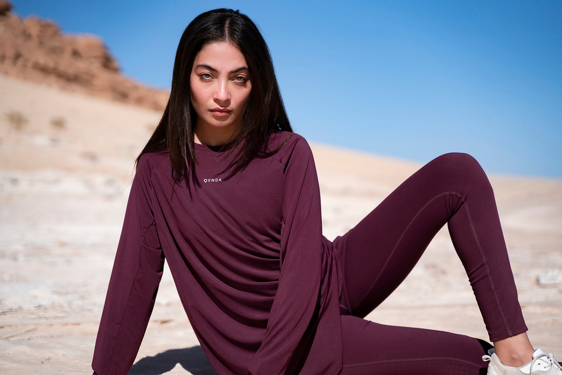 A woman poses confidently in a desert setting, with the blue sky contrasting the warm earth tones in modest activewear clothes by qynda.