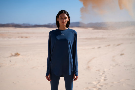A woman, wearing a high-performance blue long-sleeve Modest Workout Clothing by qynda in a vast desert landscape.