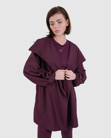A woman posing confidently in a stylish maroon COOLDOWN by Qynda coat with ruched sleeves, paired with matching trousers, set against a neutral background.