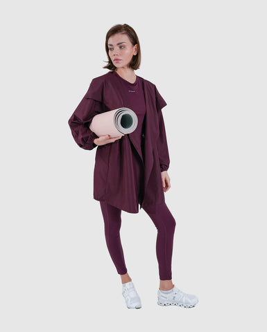 A woman in athletic holding a yoga mat, ready for a workout session, dons her cooldown coat by Qynda crafted from super light fabric.
