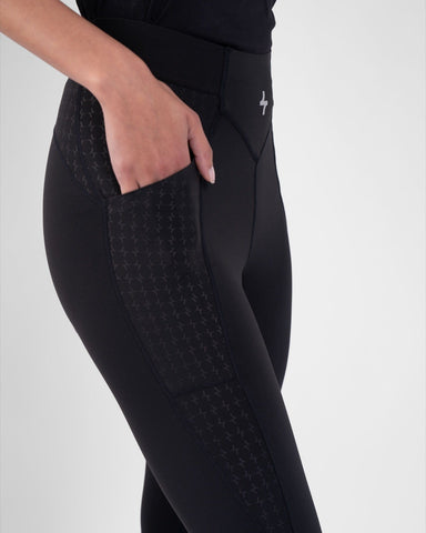 A woman showcasing the pocket feature on a pair of black modest active wear, breathable fabric athletic leggings with a patterned panel.