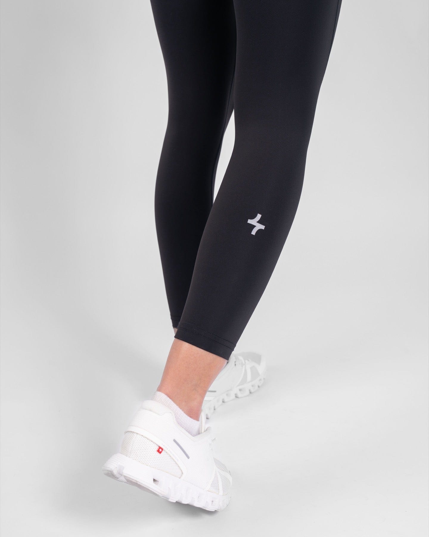 A close-up of a woman's lower legs clad in high-waisted, Black THABYA LEGGINGS and white sneakers, highlighting modest sportswear by qynda.