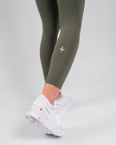 A close-up of a woman's lower legs clad in high-waisted, olive green THABYA LEGGINGS and white sneakers, highlighting modest sportswear by qynda.