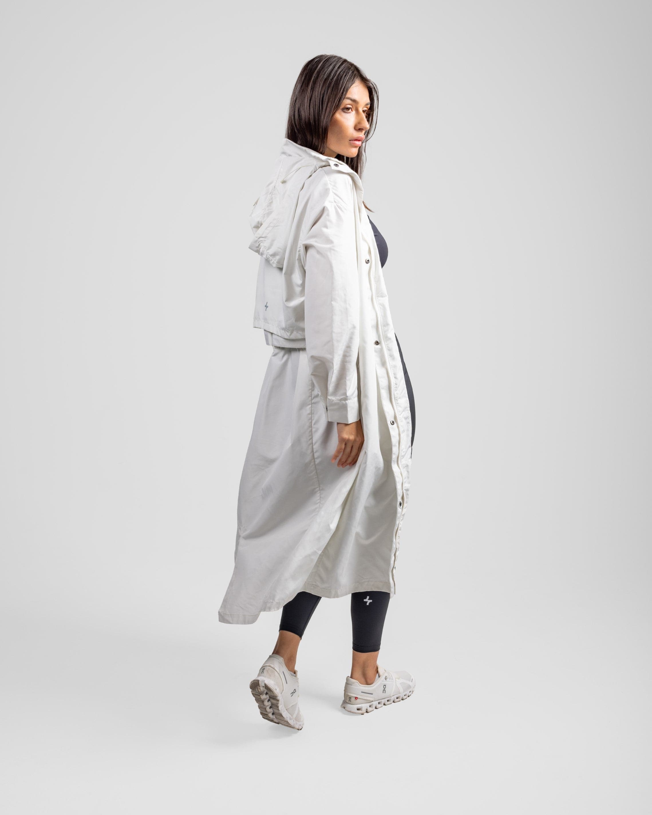 A model in a stylish modest black MAK LIGHT PARKA by Qynda with a breathable mesh lining over a dark outfit, looking back over her shoulder, set against a plain light gray background.
