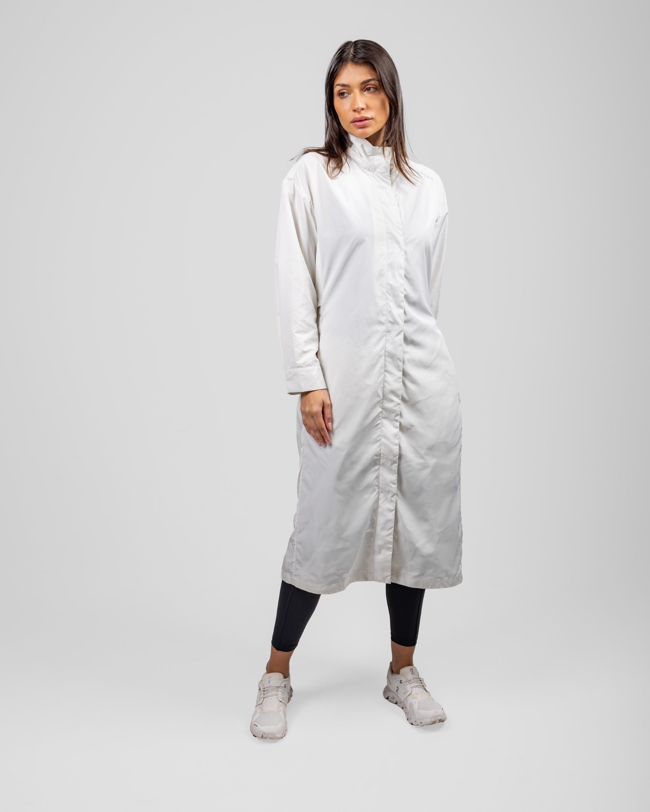 A model in a modest Off White MAK LIGHT PARKA by Qynda made of lightweight fabric and leggings, posing, standing against a light gray background.