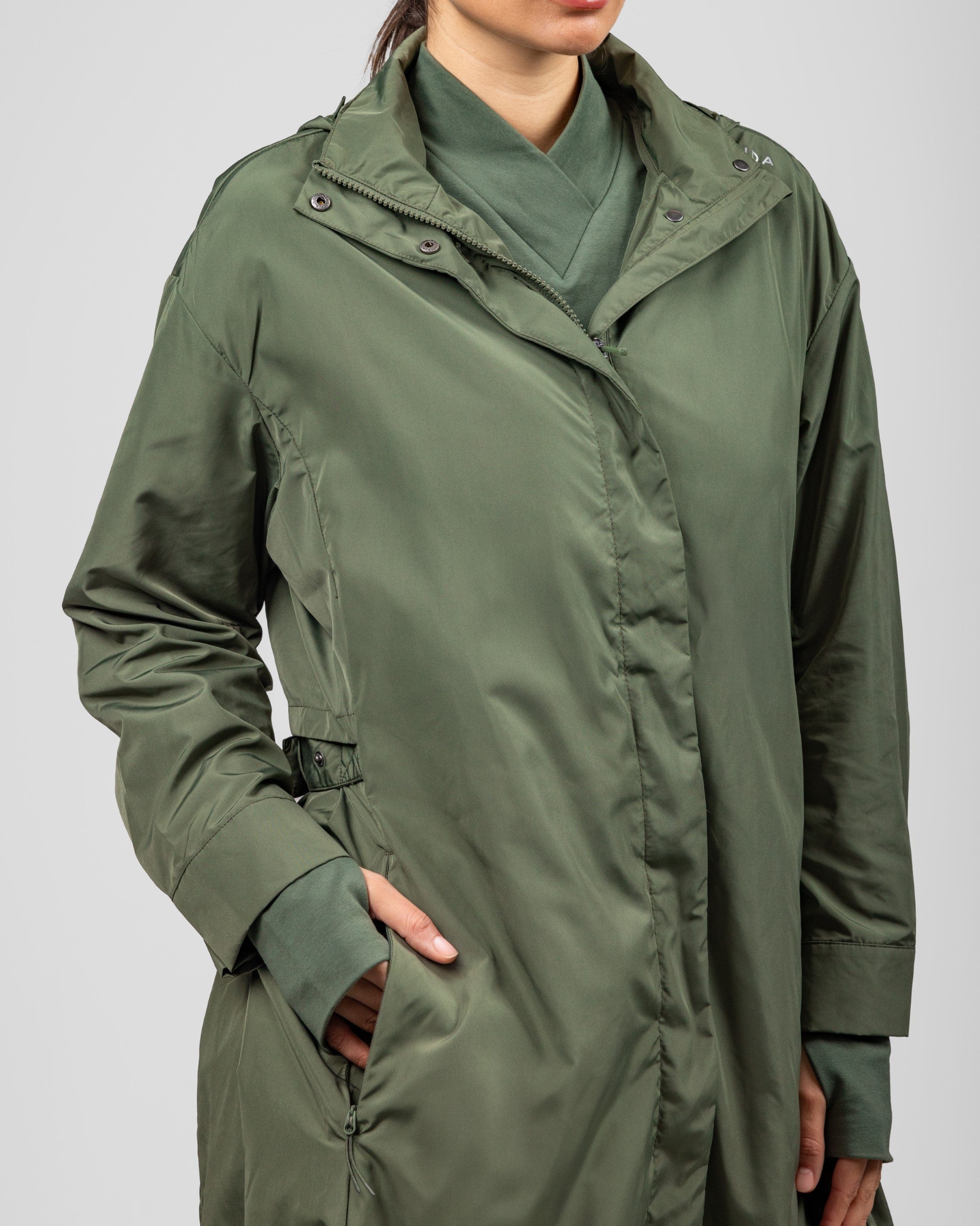 A woman models a Modest MAK LIGHT PARKA by Qynda featuring lightweight fabric, with her hand casually tucked into the pocket. Only her torso is visible against a neutral background.