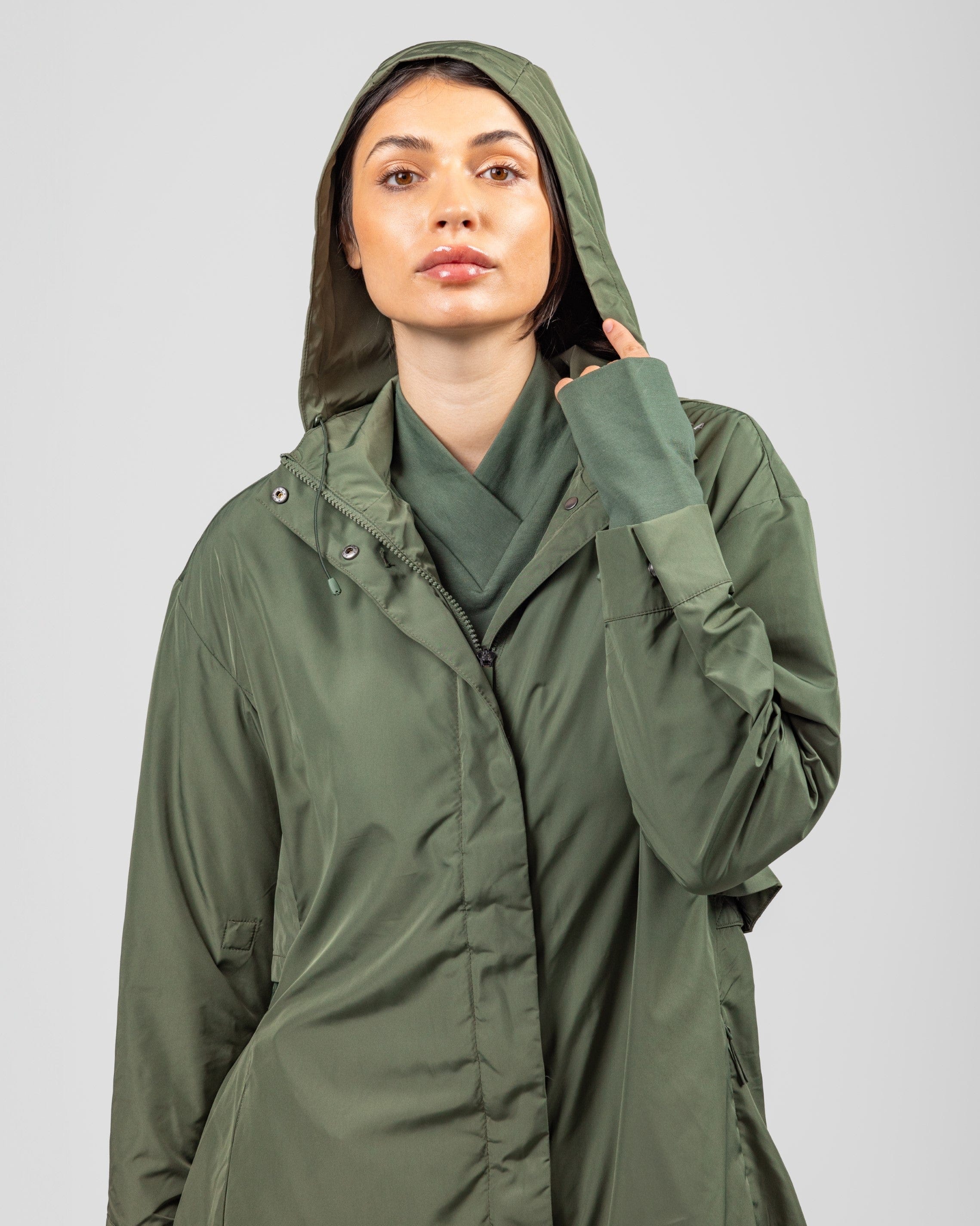 A model in a stylish olive green Modest MAK LIGHT PARKA made of lightweight fabric, with a hood, looking poised and confident.