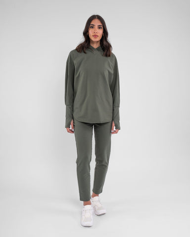 A woman stands confidently modeling modest CANTARA PANTS, Olive color made from moisture-wicking cotton terry loop fabric, complemented by a pair of white shoes.