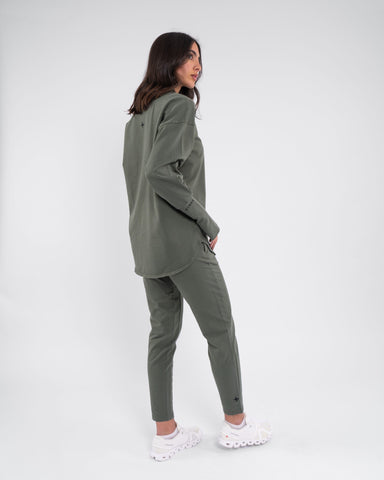 A woman in modest athletic, moisture-wicking Olive color CANTARA PANTS, by qynda stands against a plain background.