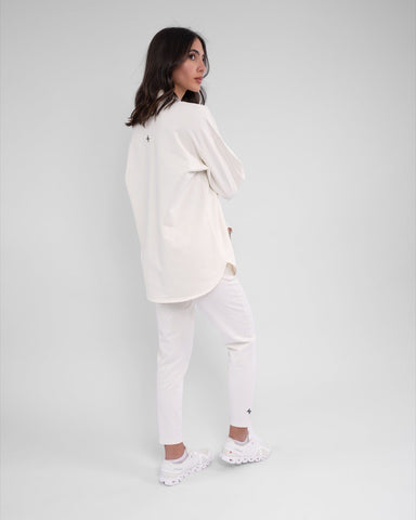 A woman in modest athletic wear moisture-wicking REHAL SWEATER and a casual off White outfit stands turned to the side, posing against a plain background.