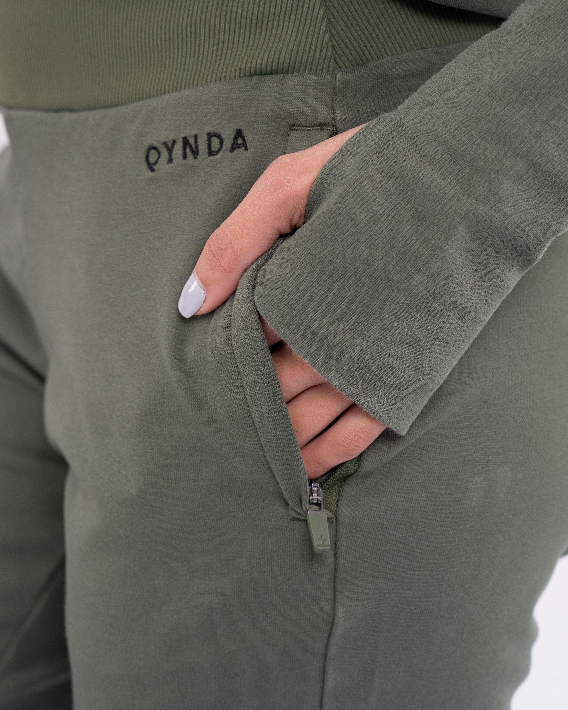 A close-up of a woman in an Olive color CANTARA PANTS with their hand in the pocket, showcasing a modern and minimalist fashion style by qynda.