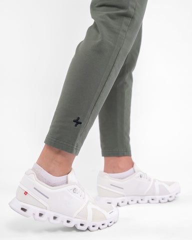 A close-up of a woman's lower legs clad in high-waisted, olive CANTARA PANTS and white sneakers, highlighting modest sportswear of qynda.