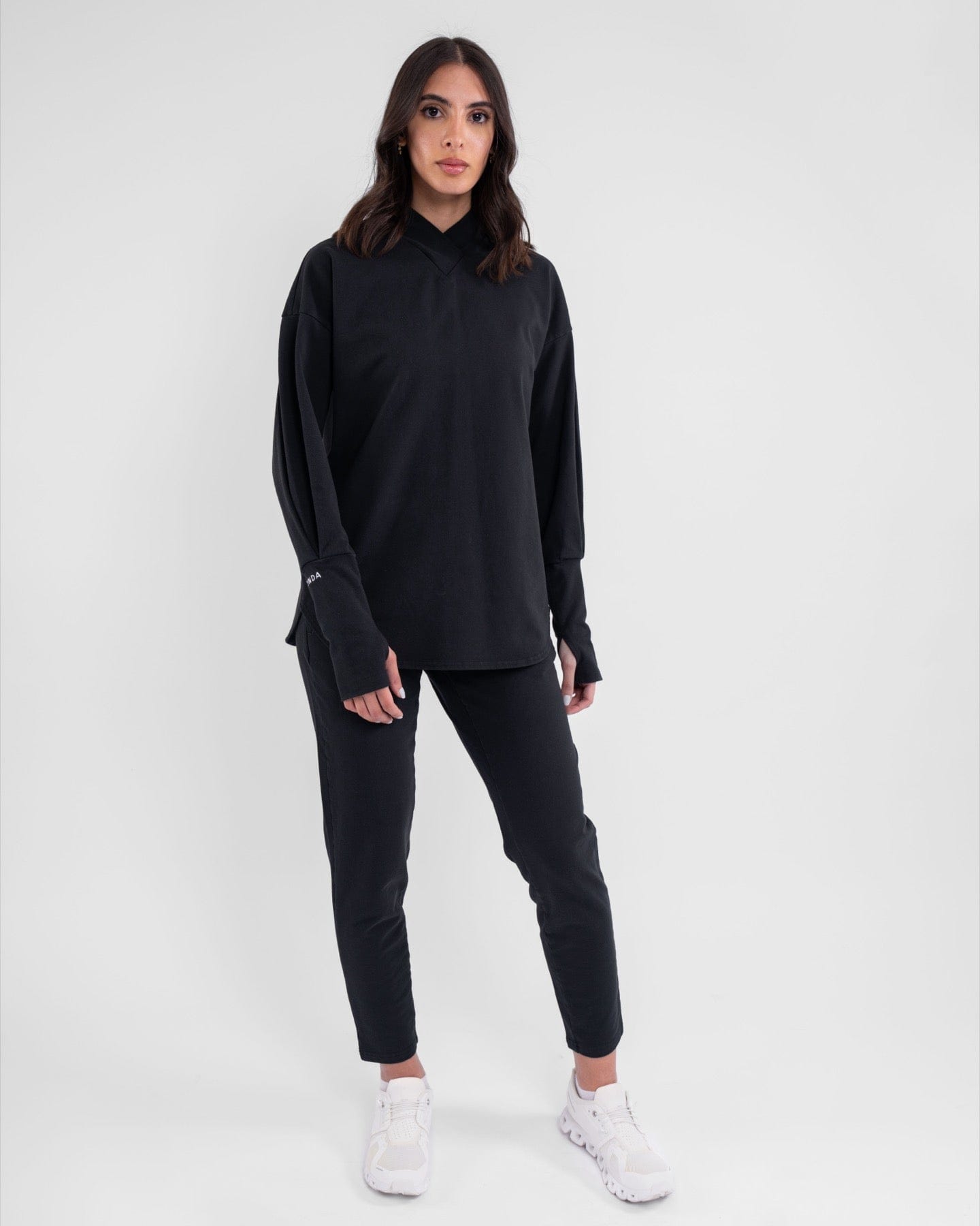 A woman stands confidently modeling a modest SWEATER by qynda and slim pants, both made from moisture-wicking cotton terry loop fabric, complemented by a pair of white shoes.