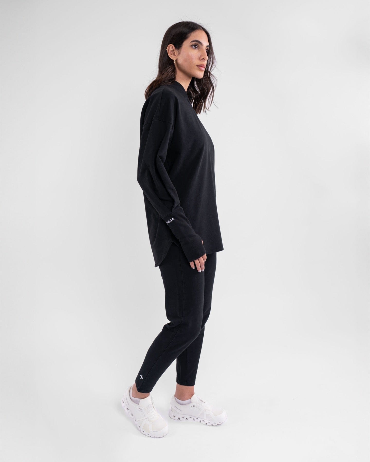 A woman in a modest athletic REHAL SWEATER by qynda and a casual Black outfit stands against a plain background.