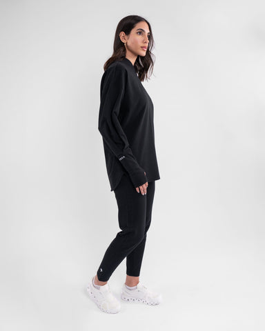 A woman in modest athletic, moisture-wicking CANTARA PANTS joggers and a casual Black outfit stands against a plain background.