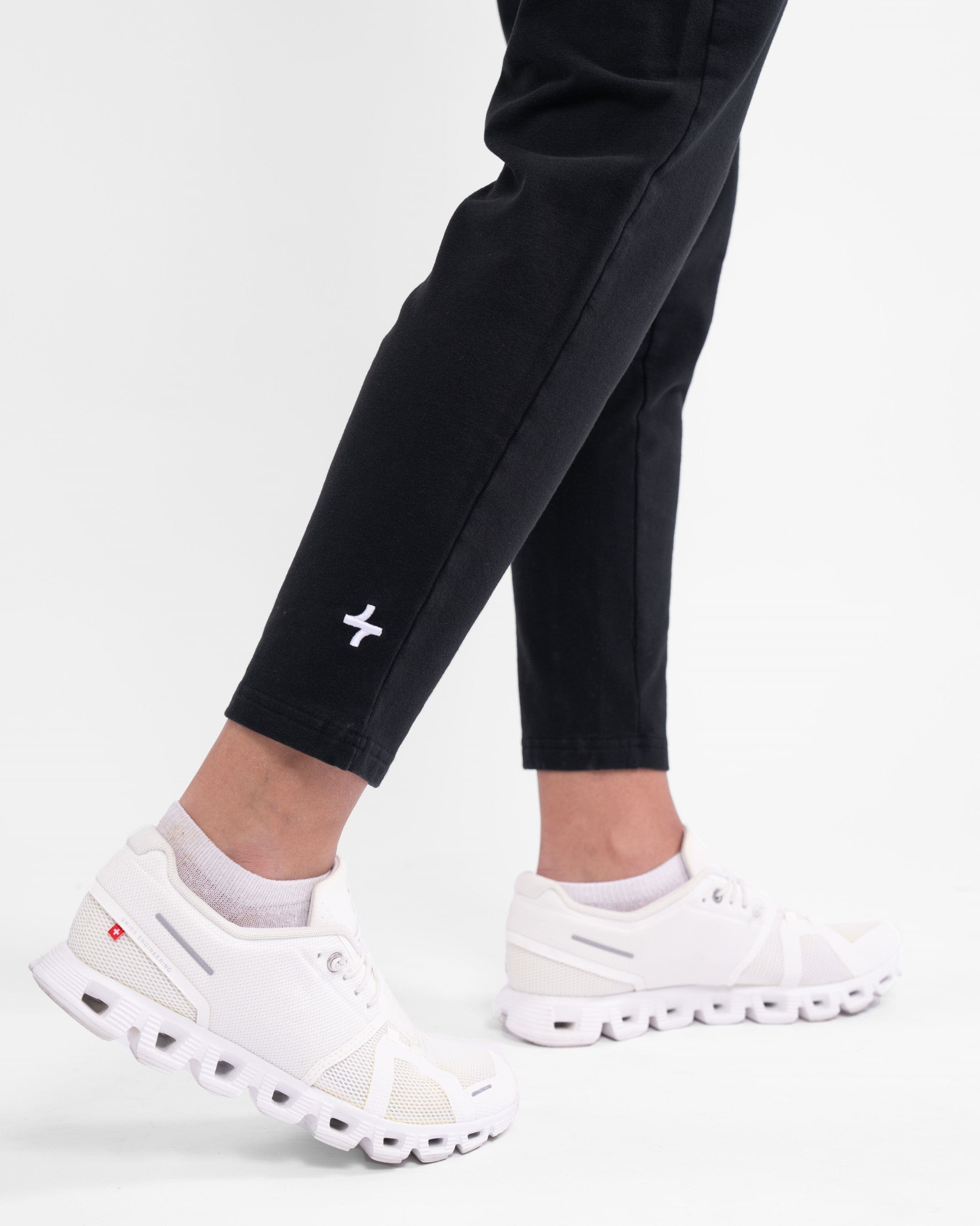 A close-up of a woman's lower legs clad in high-waisted, black CANTARA PANTS and white sneakers, highlighting modest sportswear of qynda.