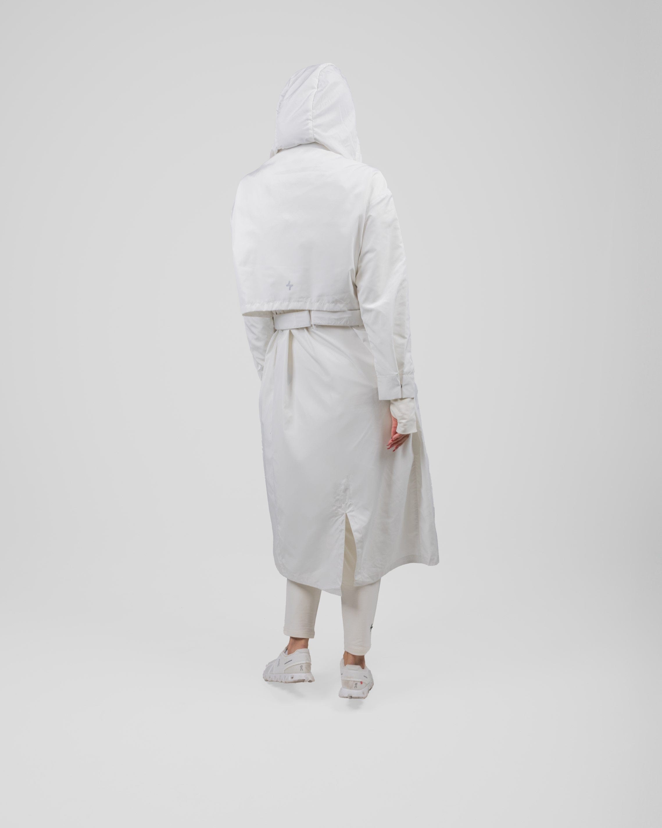 A model from behind wearing a Off White MAK LIGHT PARKA by Qynda with a hood and white breathable mesh sneakers, walking to the right on a plain light gray background.
