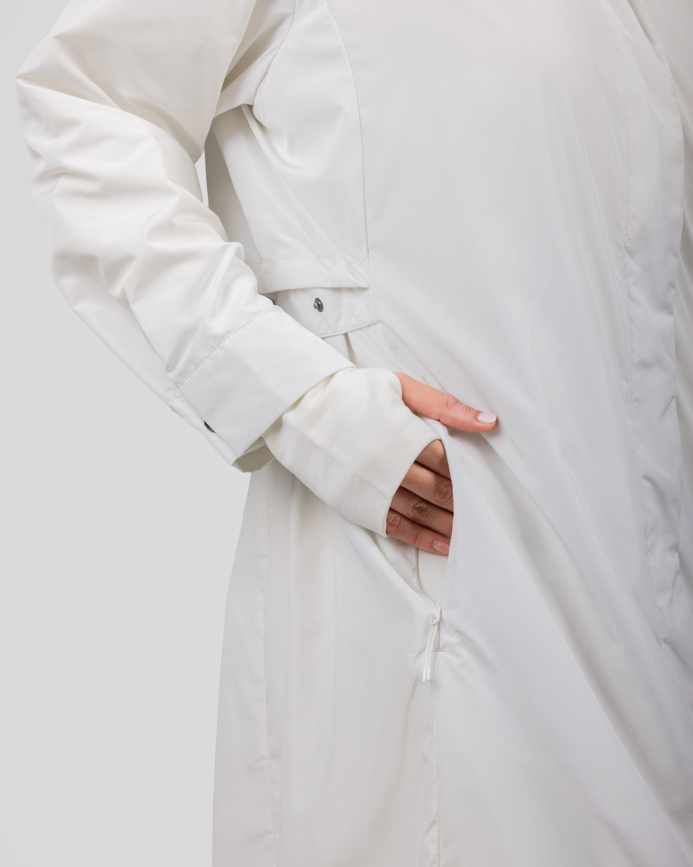 A close-up image of a model wearing modest Off White MAK LIGHT PARKA by Qynda coat crafted from lightweight fabric, inserting their hand into a side pocket. 