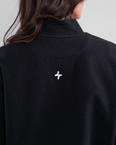 Close-up of the back of a woman's black modest activewear top with a qynda logo embroidered near the neckline.
