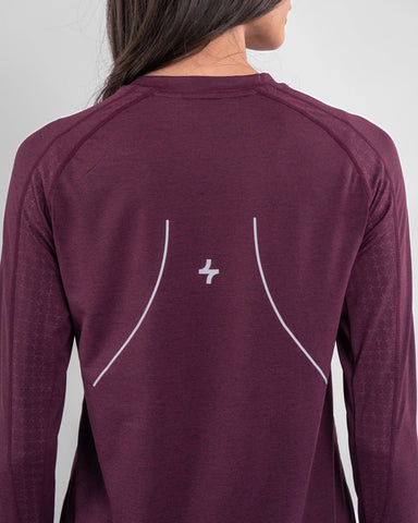 A woman from behind wearing a Maroon OFOQ LONG SLEEVE T-SHIRT, crafted with brrr° material for moisture resistance and body temperature regulation, showcases a qynda logo on the upper back.