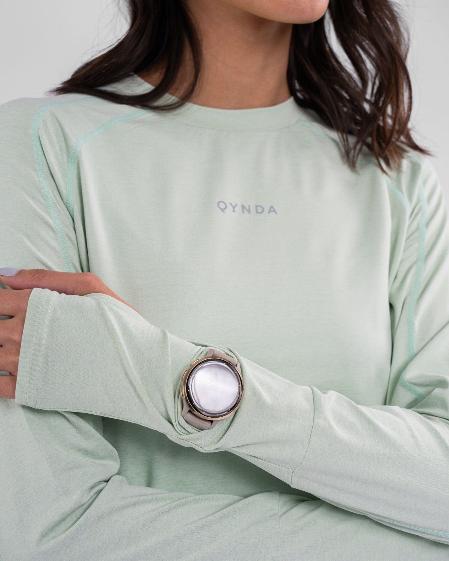 A woman in a modest athletic top with a qynda brand logo, made from moisture-resistant and quick-drying fabric, complemented by a large silver ring with a white stone on the index finger.