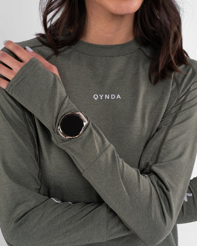 A woman in a modest athletic OFOQ LONG SLEEVE T-SHIRT with a qynda brand logo, made from moisture-resistant and quick-drying fabric.