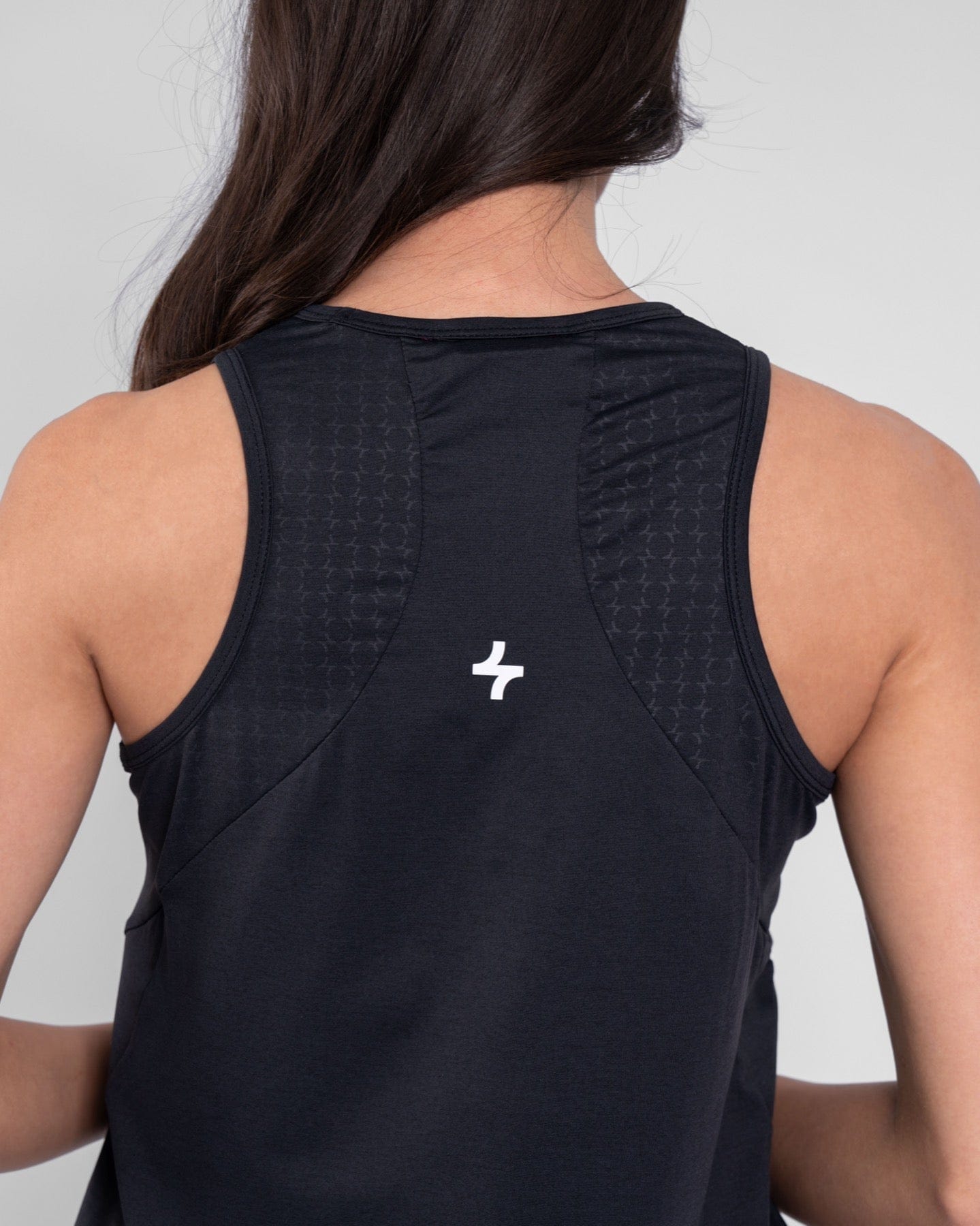 A woman from behind wearing a Black RUH TANK TOP, crafted with brrr° material for moisture resistance and body temperature regulation, showcases a qynda logo on the upper back.