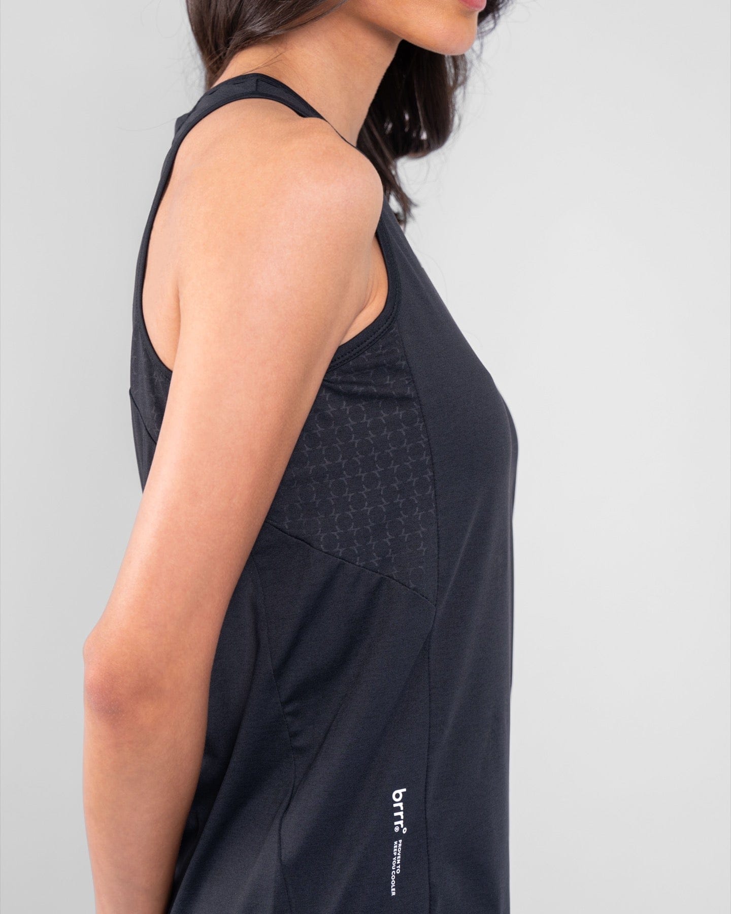 Woman showcasing the side and back details of a black RUH TANK TOP by qynda with a subtle patterned fabric, moisture resistance.