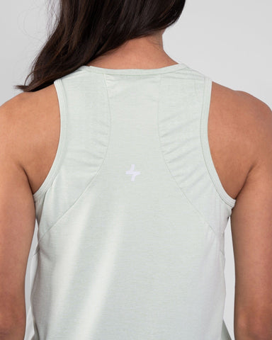 A woman from behind wearing a sage tank top, crafted with brrr° material for moisture resistance and body temperature regulation, showcases a qynda logo on the upper back.