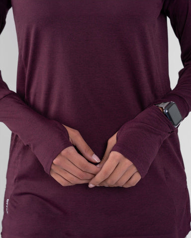 A woman in a modest athletic OFOQ LONG SLEEVE T-SHIRT with a qynda brand logo, made from moisture-resistant and quick-drying fabric, complemented by a large silver watch on the wrist.
