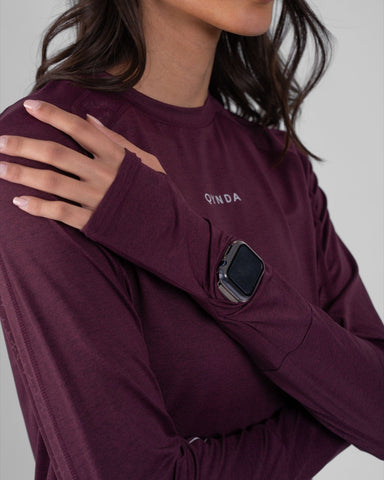 A woman in a modest athletic top with a qynda brand logo, made from moisture-resistant and quick-drying fabric, complemented by a large silver ring on the wrist.