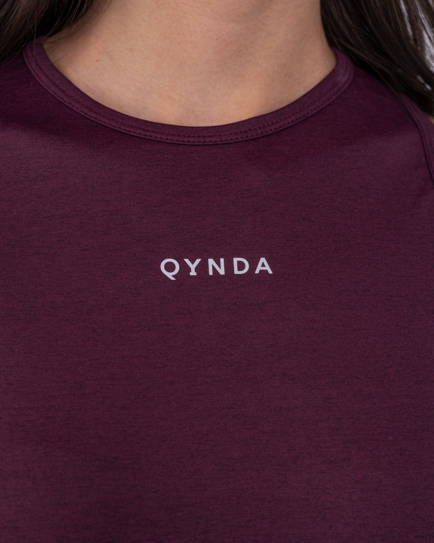A woman with a modest athletic top made of brrr° material, with the brand "qynda" on it, looking.