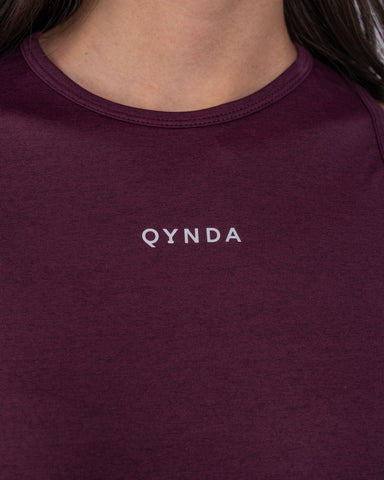 A woman with a modest athletic top made of brrr° material, with the brand "qynda" on it, looking.