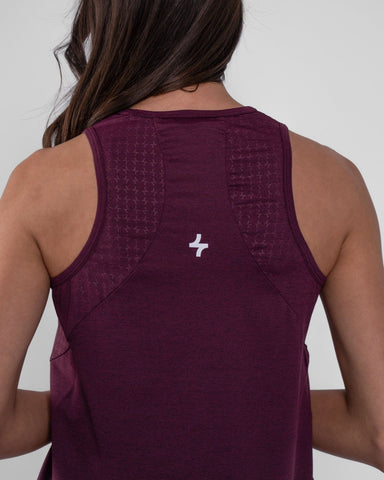 A woman from behind wearing a Maroon tank top, crafted with brrr° material for moisture resistance and body temperature regulation, showcases a qynda logo on the upper back.