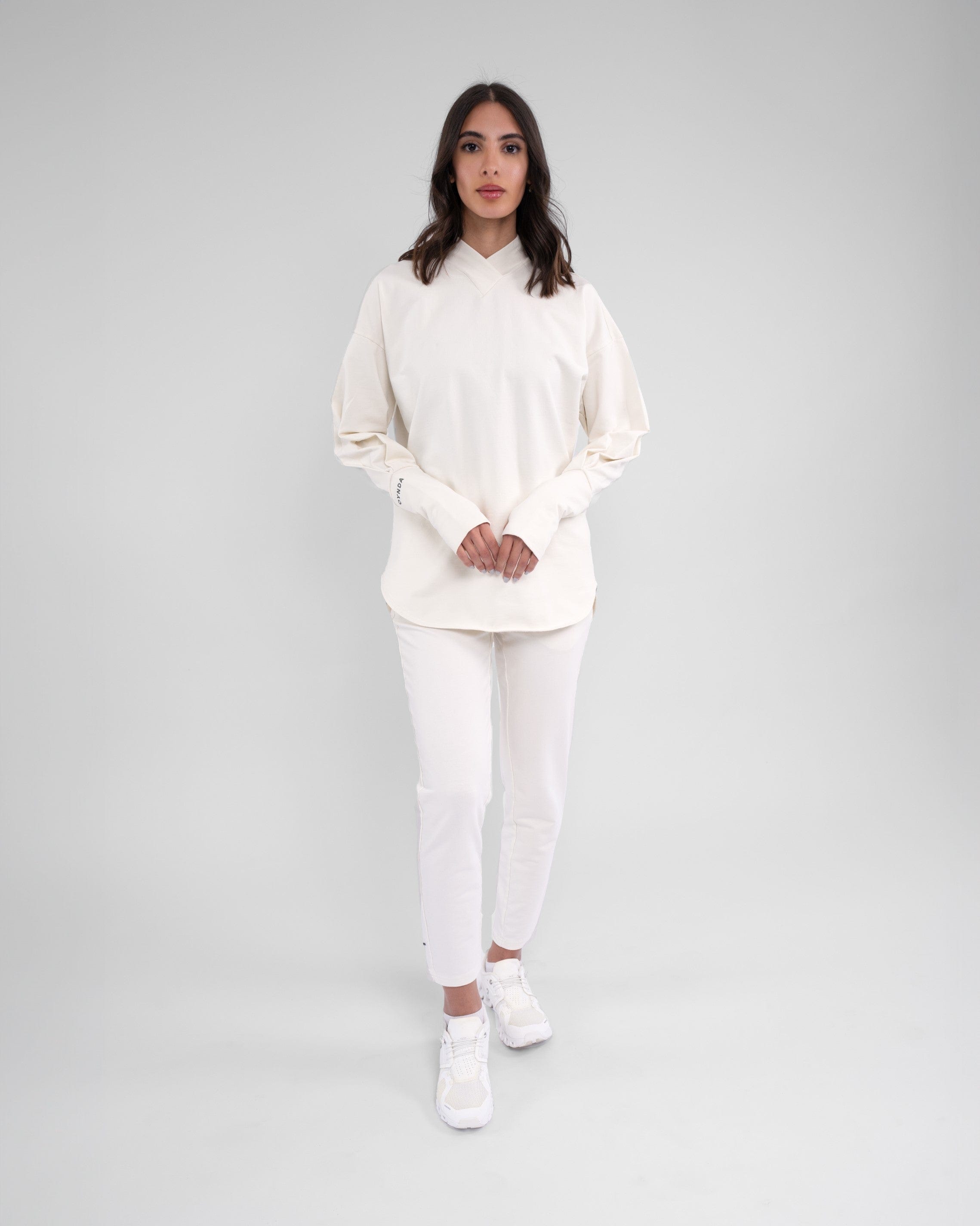 A woman stands confidently modeling modest CANTARA PANTS, Off White color made from moisture-wicking cotton terry loop fabric, complemented by a pair of white shoes.