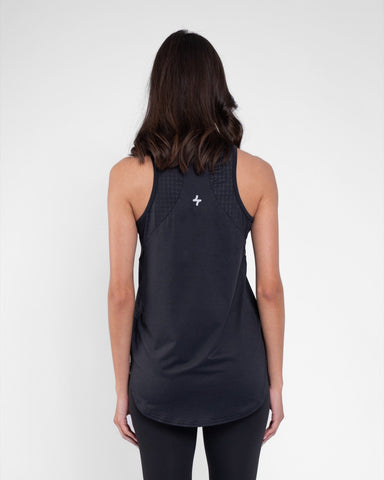 A woman standing with her back turned towards the camera, wearing a Black modest activewear, sleeveless athletic top and matching leggings against a neutral gray background