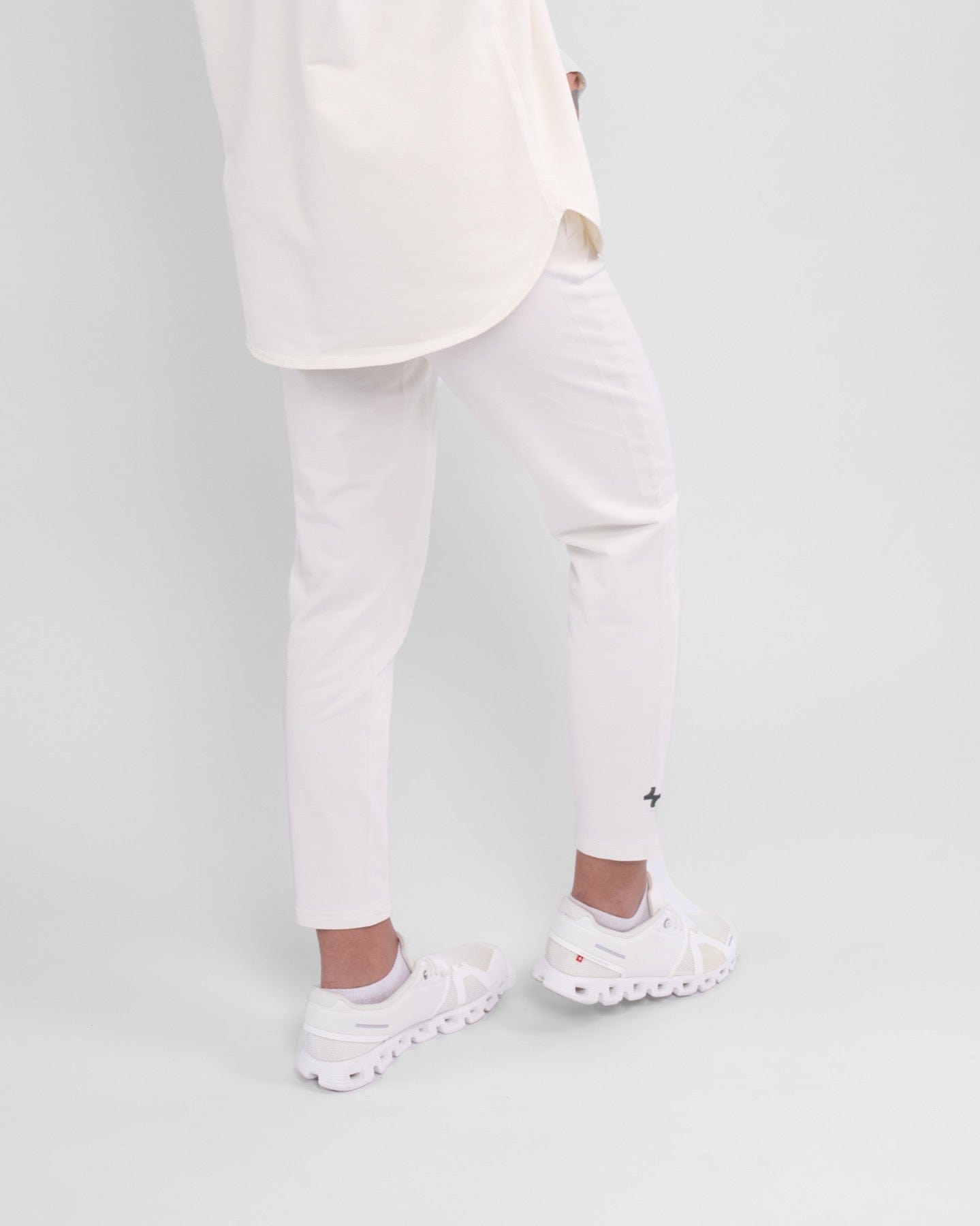 A close-up of a woman's lower legs clad in high-waisted, Off White CANTARA PANTS and white sneakers, highlighting modest sportswear by qynda.
