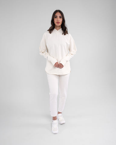 A woman stands confidently modeling modest CANTARA PANTS, Off White color made from moisture-wicking cotton terry loop fabric, complemented by a pair of white shoes.