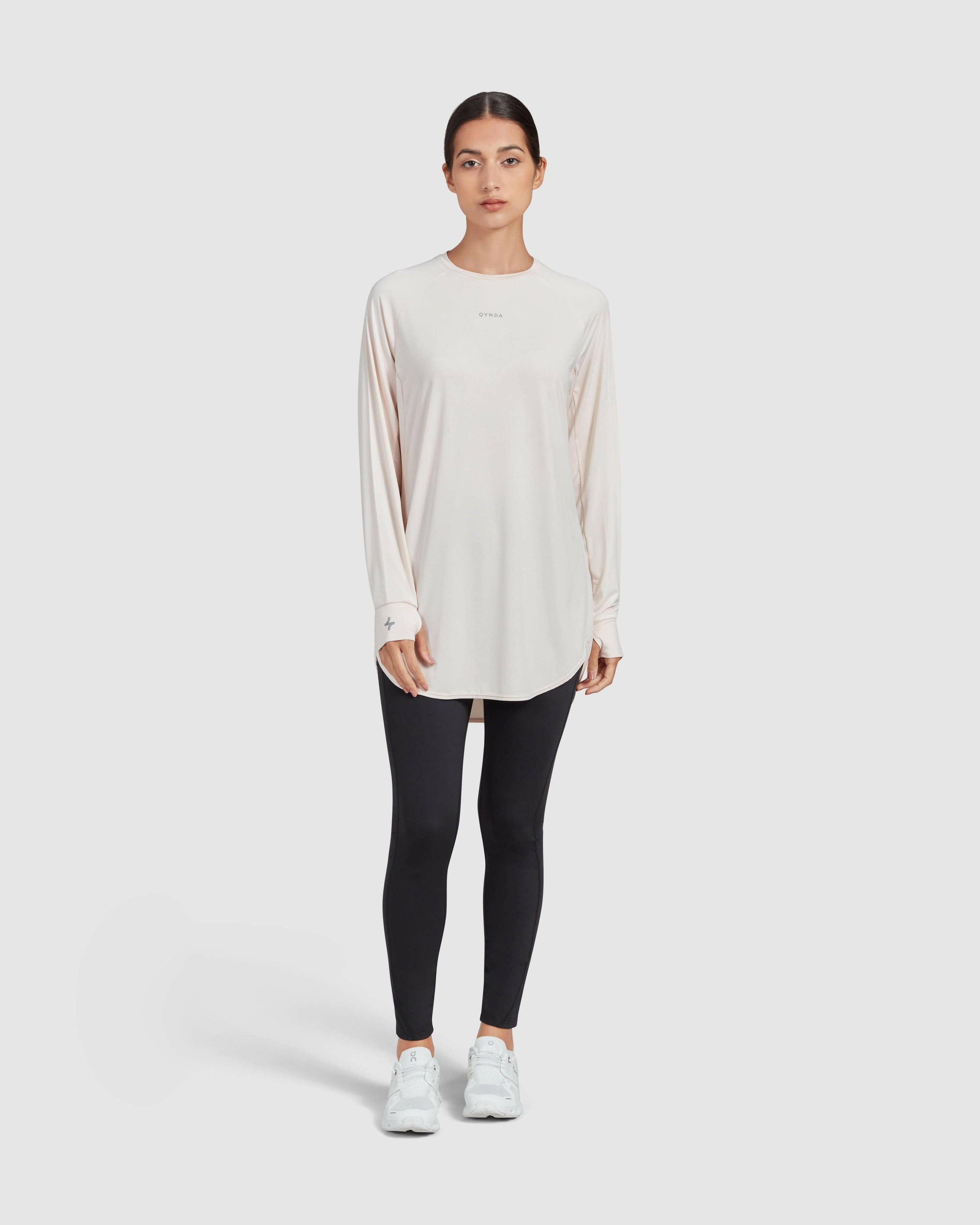 A model stands against a white background, dressed in a modest shell MOD LONG SLEEVE T-SHIRT and black leggings