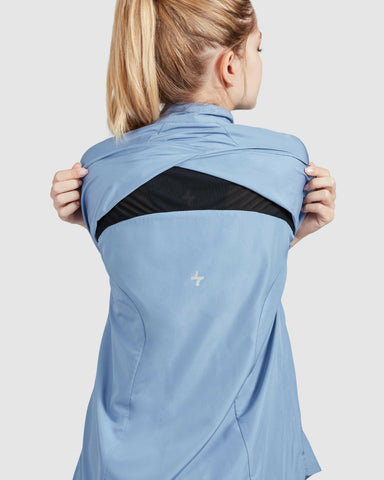 A model from behind stretching a light blue FLY JACKET by Qynda to showcase its flexible back vent feature for enhanced air flow.