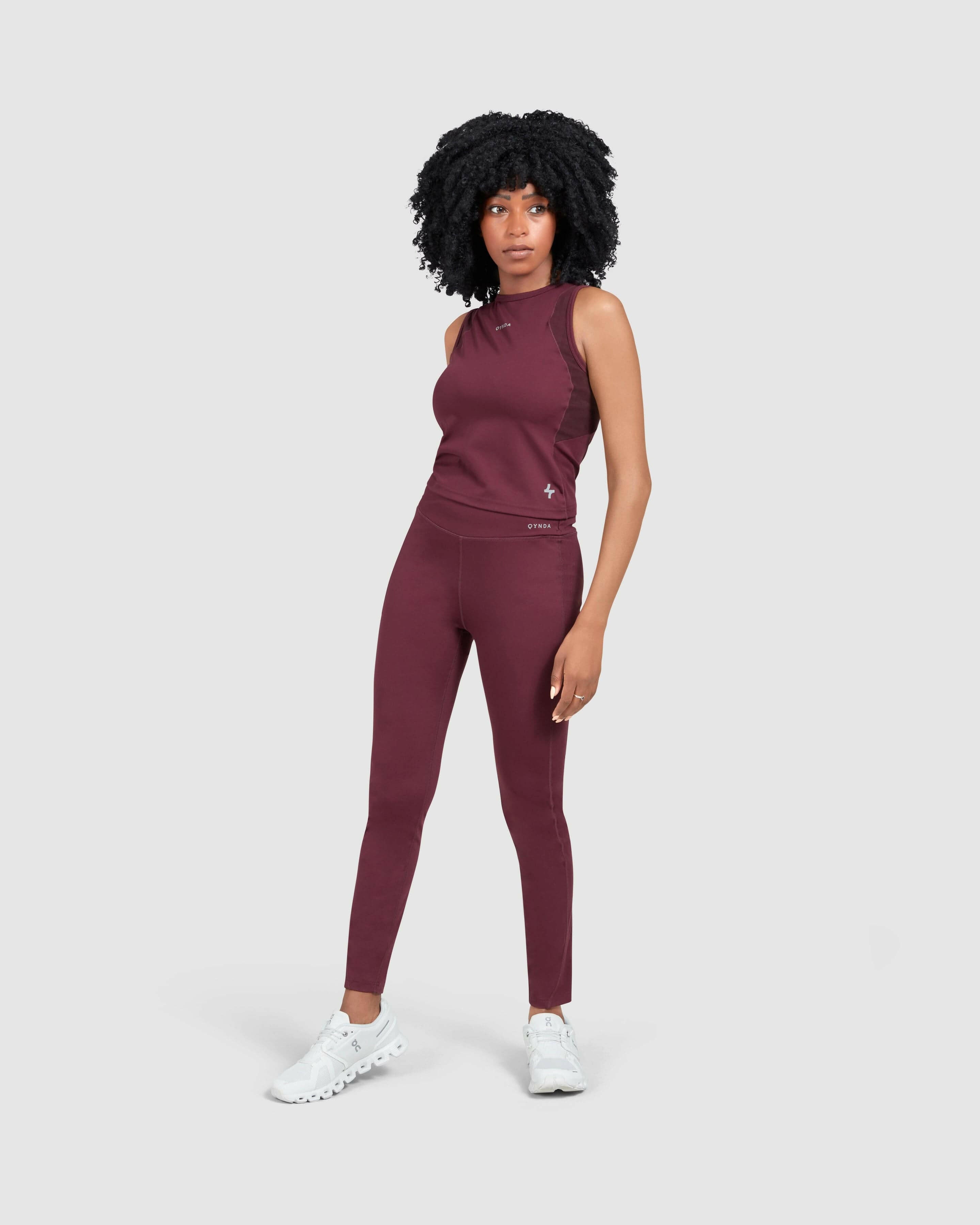 A model stands confidently, modeling a Maroon and matching Modest LADINA LEGGINGS from QYNDA, complemented by white sneakers, against a clean white background.
