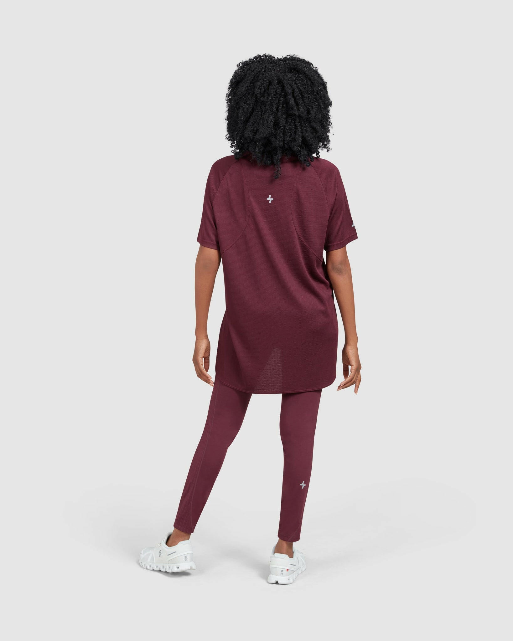 Woman seen from behind, wearing a maroon short-sleeved BREATHE T-SHIRT with Qynda brand logo and matching leggings, paired with white sneakers for maximum breathability.