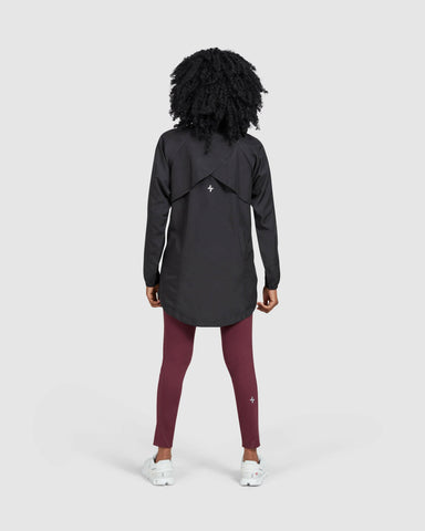 A model seen from behind, standing against a neutral background, wearing a black FLY JACKET by Qynda with a hidden mesh back and both ways zipper and maroon leggings.