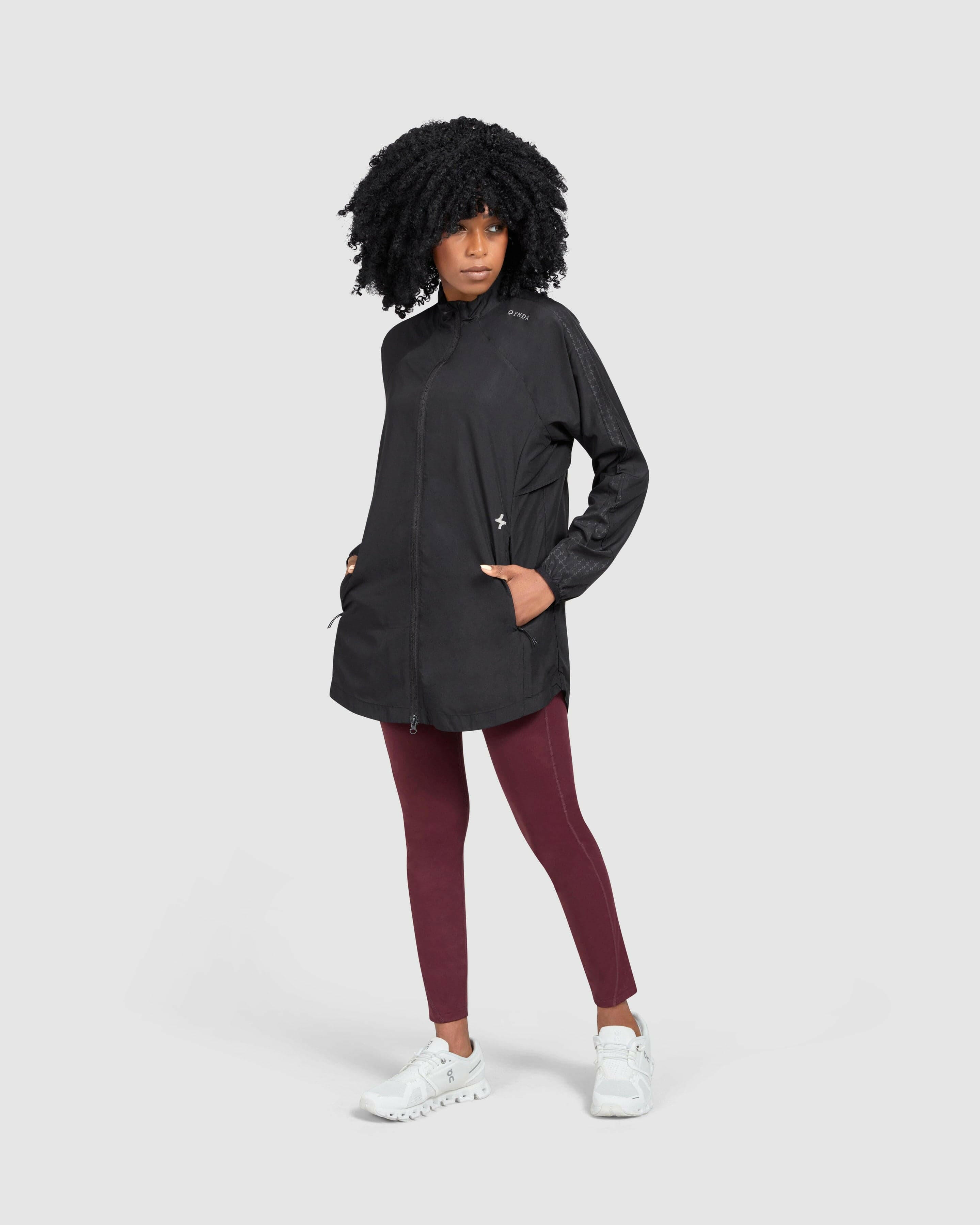 A confident model in FLY JACKET crafted from super light fabric and maroon leggings paired with white sneakers poses with her hand on her hip against a neutral background.