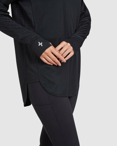 A woman clad in activewear featuring a long-sleeve black QYNDA active t-shirt with a thumb hole in the cuffs and black leggings, focusing on the details and fit of the sporty.