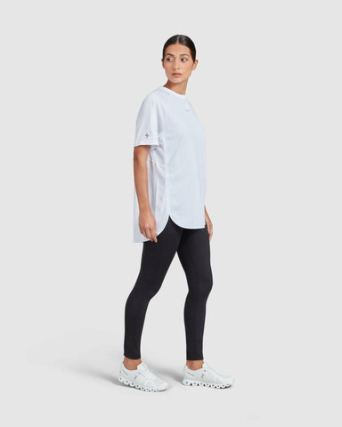 A woman in a white short sleeve t-shirt and black leggings standing against a white background, giving a side pose while gazing into the distance, exemplifying a casual, sporty, and breathable look