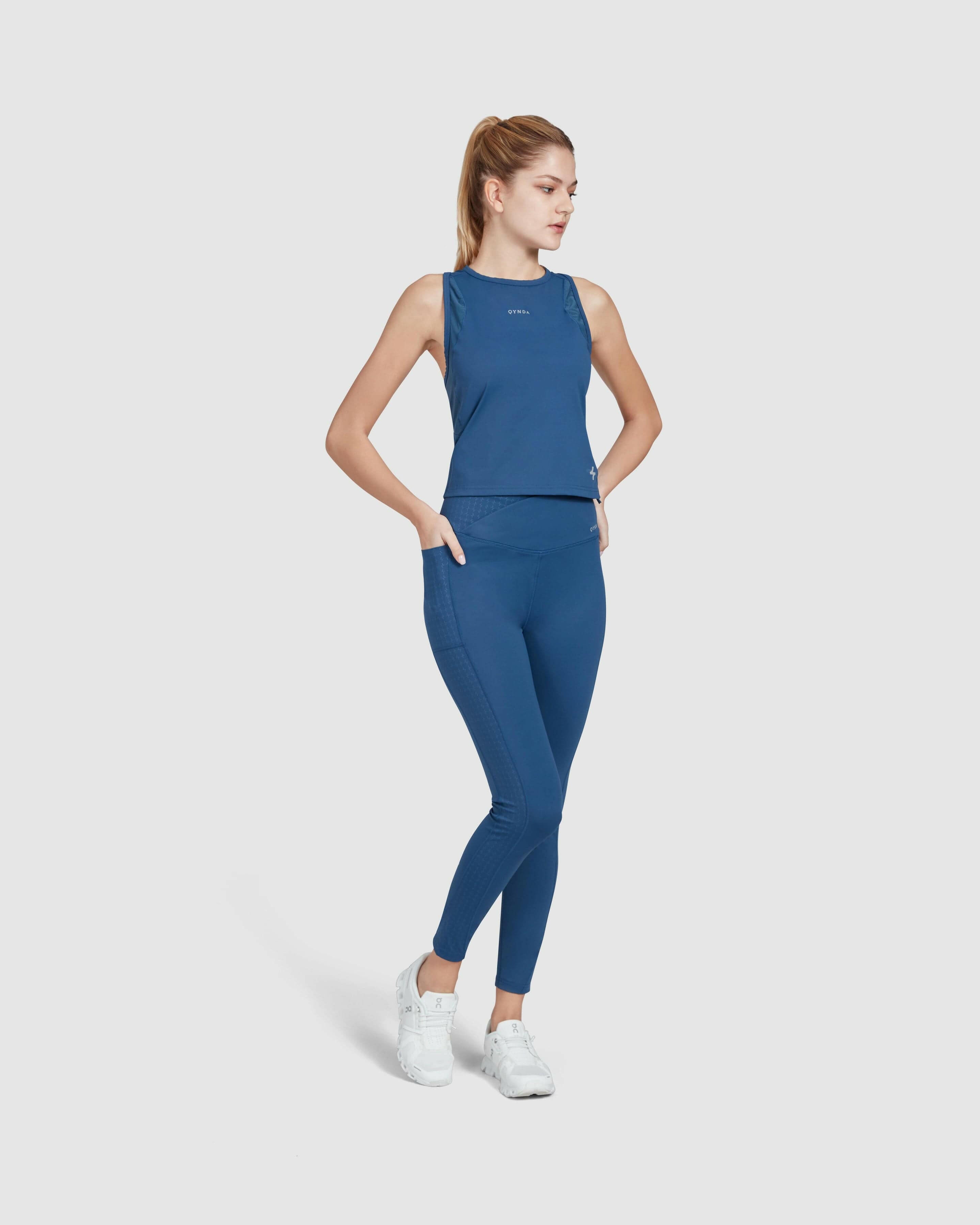 A model stands confidently, modeling Dark Denim color and matching Modest LADINA LEGGINGS from QYNDA, complemented by white sneakers, against a clean white background.