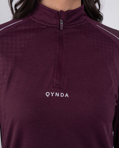 Close-up of a woman wearing a maroon color, high-neck sleeve shirt ARMA by Qynda with a subtle hexagonal pattern, featuring a half-zip.