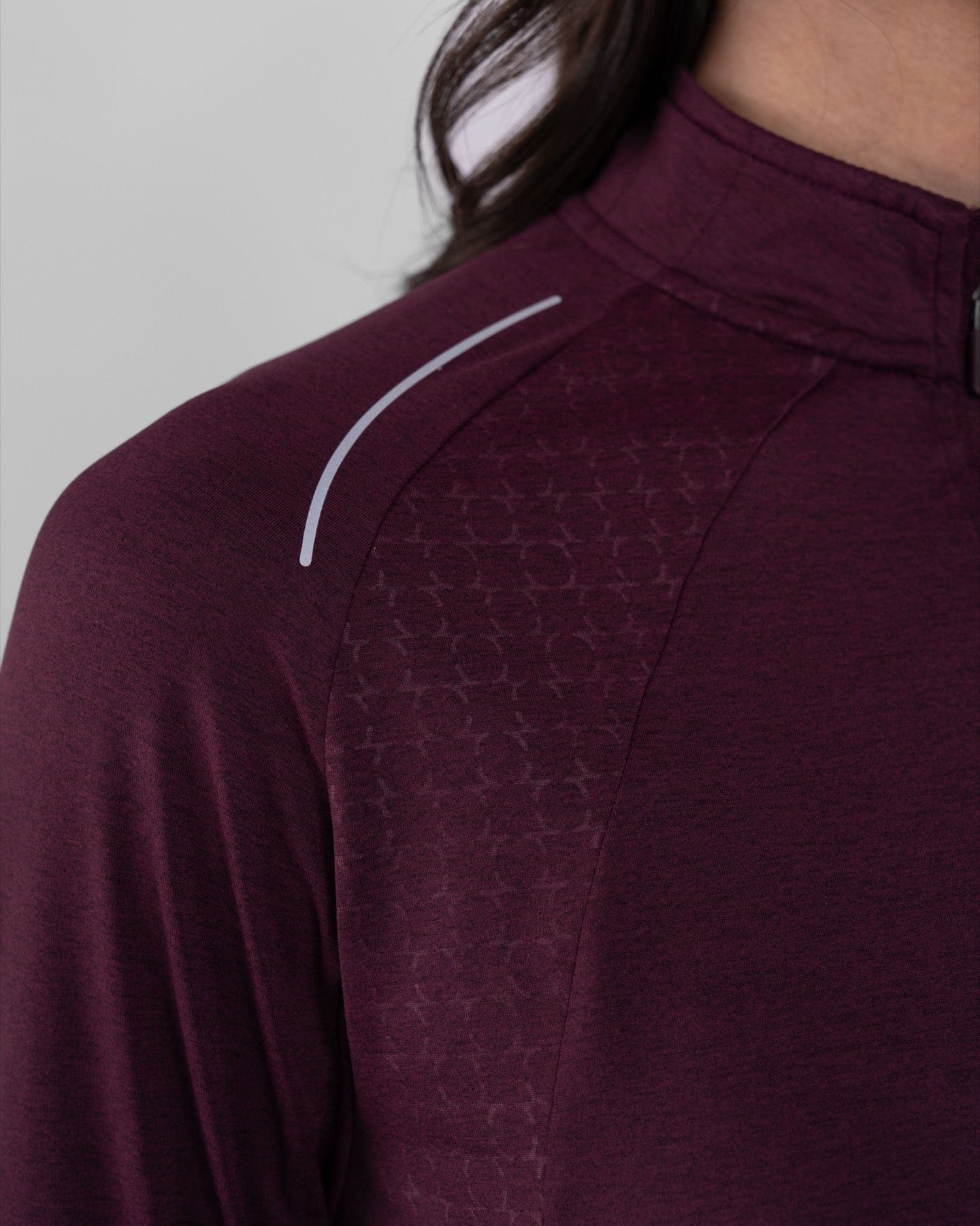 Close-up of the shoulder detail on a high neck long sleeve shirt ARMA by Qynda, featuring a moisture-resistant textured fabric pattern and a curved white reflective stripe.